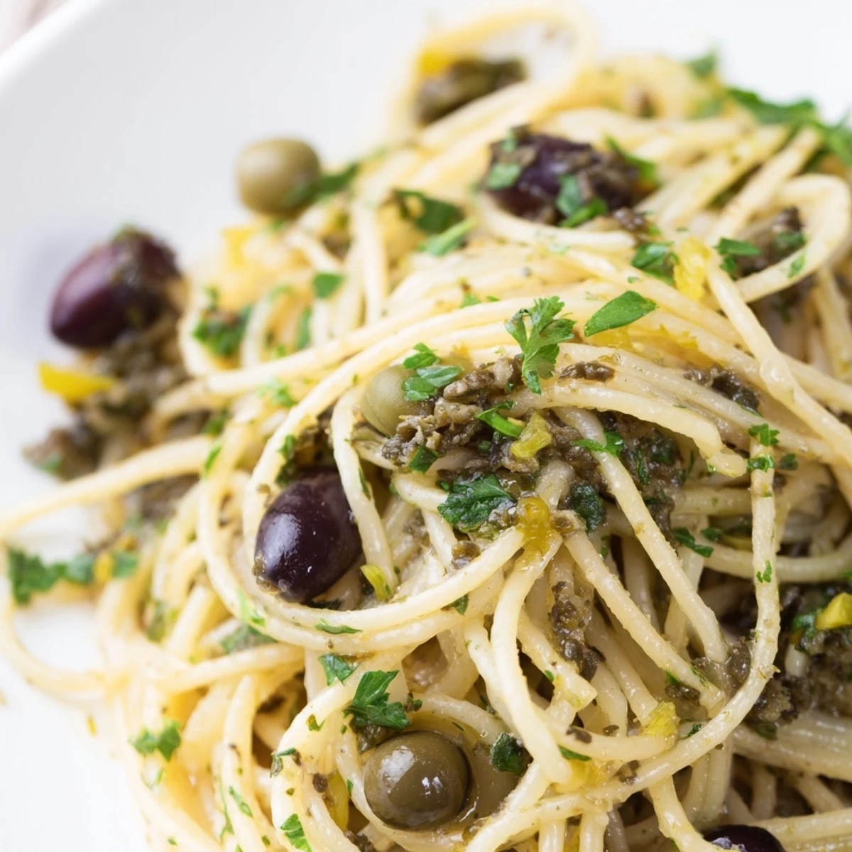 Close-up of Olive Tapenade Pasta with a chunky olive and caper sauce tossed through al dente spaghetti, garnished with fresh parsley and lemon zest.