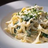 Vibrant spinach mixed with creamy fettuccine Alfredo, garnished with fresh parsley and Parmesan cheese.