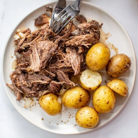 Tender slow cooker pot roast, falling apart with potatoes, rich broth visible in the crock pot.