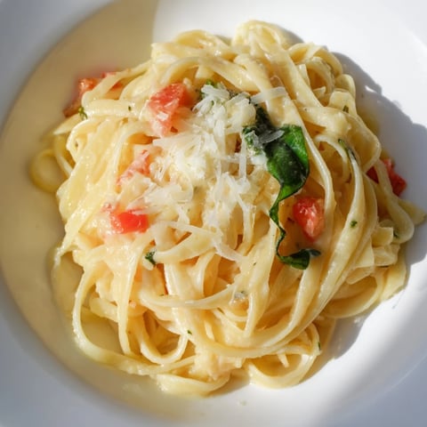 A close-up of creamy Roasted Garlic Pasta Sauce tossed with spaghetti, garnished with fresh basil and grated Parmesan.