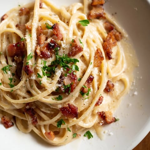 Crispy Bacon Linguine is plated on a white dish, showcasing golden, crispy bacon bits nestled in glossy linguine strands.