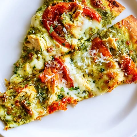 A golden, thin-crust Chicken Pesto Pizza fresh from the oven, topped with melted mozzarella, juicy tomato slices, and fresh basil garnish.  