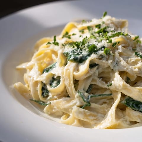 Vibrant spinach mixed with creamy fettuccine Alfredo, garnished with fresh parsley and Parmesan cheese.