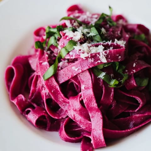 Sliced beet noodle pasta plated with grated Parmesan and basil, highlighting the homemade pasta’s rich, earthy pink hue.