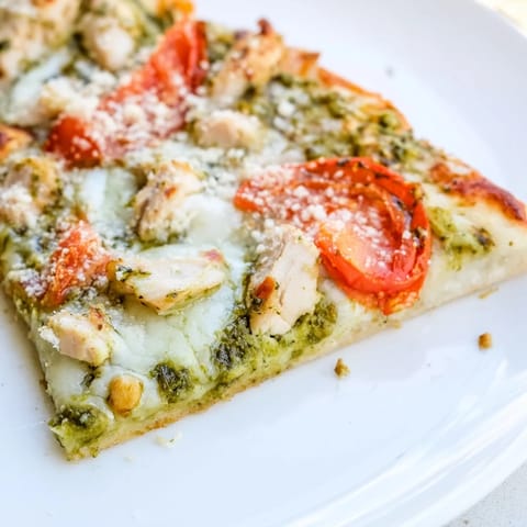 Golden-brown Chicken Pesto Pizza on a rustic wooden board, featuring vibrant green pesto, tender chicken pieces, and melted cheese.  