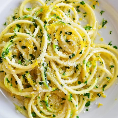 Lemon Zucchini Pasta is plated with golden edges, featuring tender zoodles mingling with pasta, a glossy lemony butter glaze, and a sprinkle of red pepper flakes.