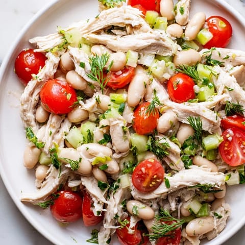 Shredded chicken, white beans, cherry tomatoes, and herbs in Lemony White Bean Chicken Salad, plated over crisp lettuce leaves.