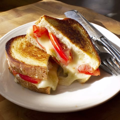 Two halves of a Pepper Jack & Tomato Grilled Cheese sandwich on a plate, served alongside a creamy bowl of tomato soup.
