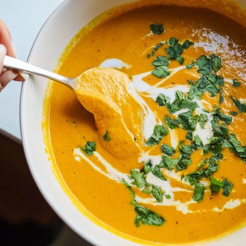 Creamy Carrot Ginger Soup in a white bowl, swirled with coconut cream and chopped parsley.  