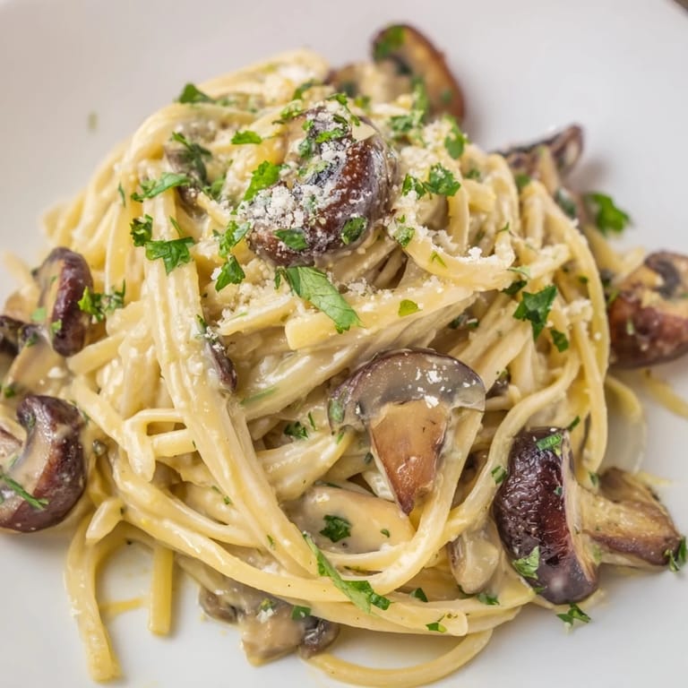 Golden sautéed mushrooms and fresh parsley garnish a bowl of Creamy Mushroom Linguine, glistening with light cream sauce.