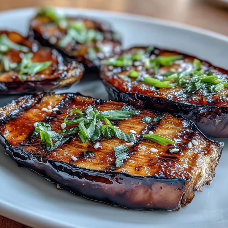 Golden-brown eggplant halves with a bubbling miso glaze, garnished with sesame seeds and green onions for a flavorful Japanese-inspired dish.