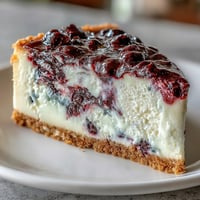 A creamy black currant cheesecake with a buttery graham cracker crust and tangy berry swirls, perfect for dessert lovers.  