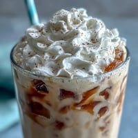 Creamy vanilla frappuccino with cold brew ice cubes in a tall glass, topped with whipped cream and a drizzle of vanilla bean paste.